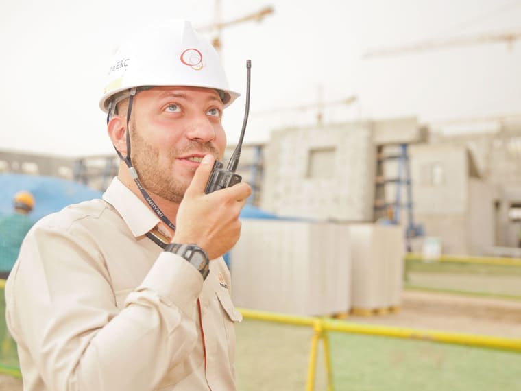 A site supervisor in a hard hat using a two-way radio