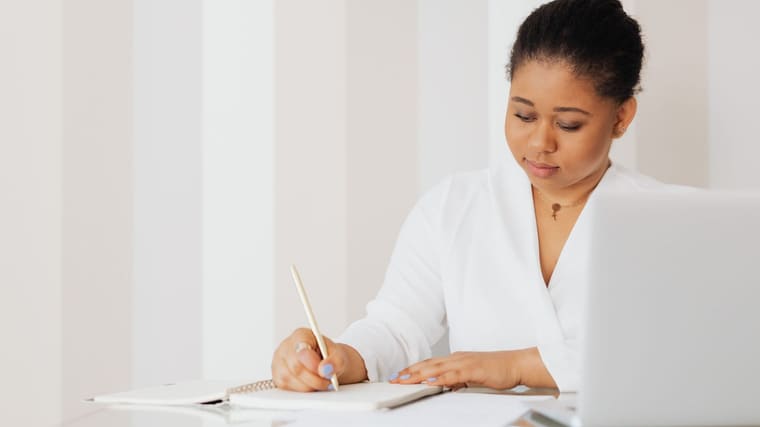 A reader taking notes beside a laptop